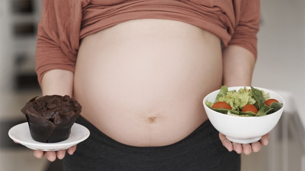 Pregnant woman with a salad in her left hand and a chocolate muffin in the left.