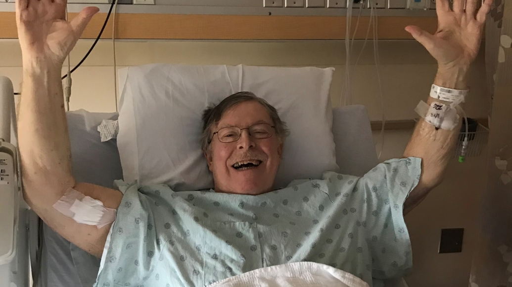 older man holding hands up over head celebrating in hospital bed 