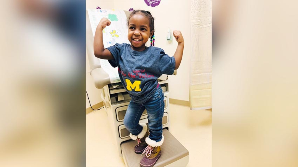 little girl doing muscle pose in doctor&#039;s office wearing a blue Michigan shirt
