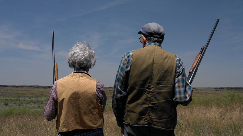 older couple in field holding shot guns