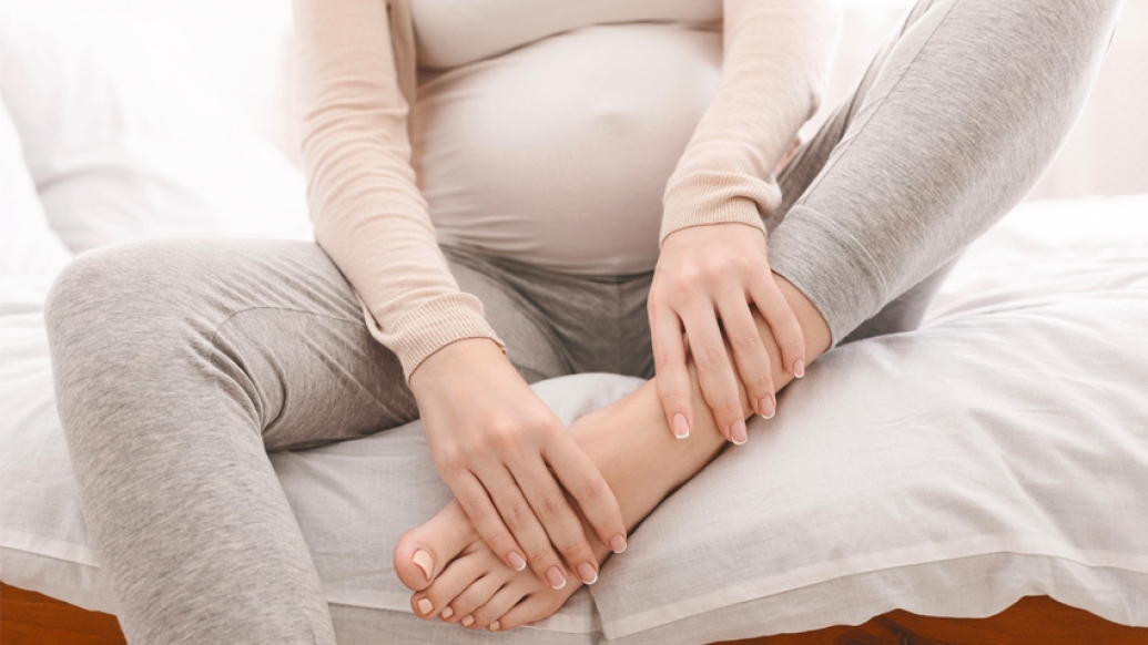 pregnant person holding feet on bed grey sweats