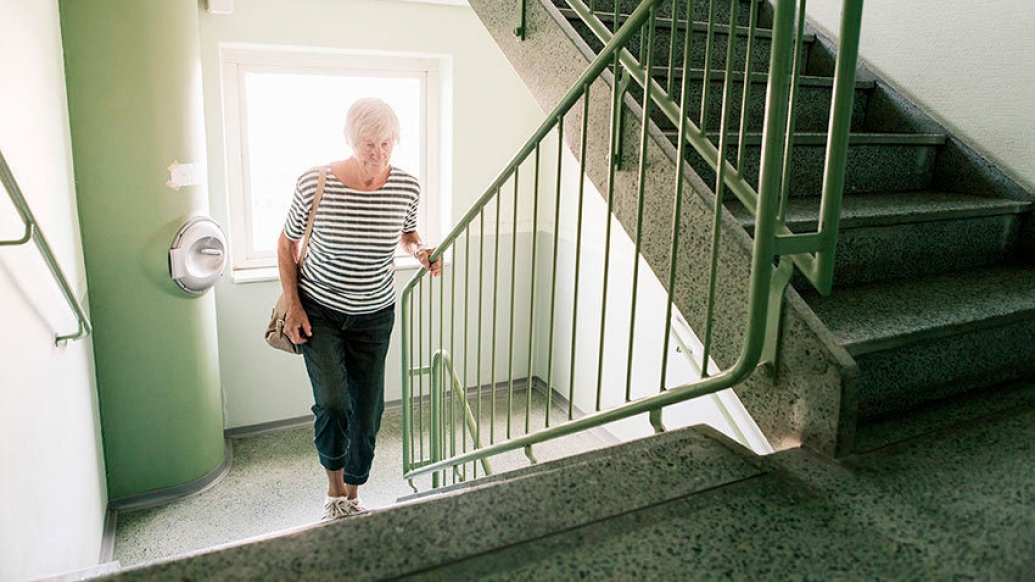 senior woman climbs stairs and holds railing