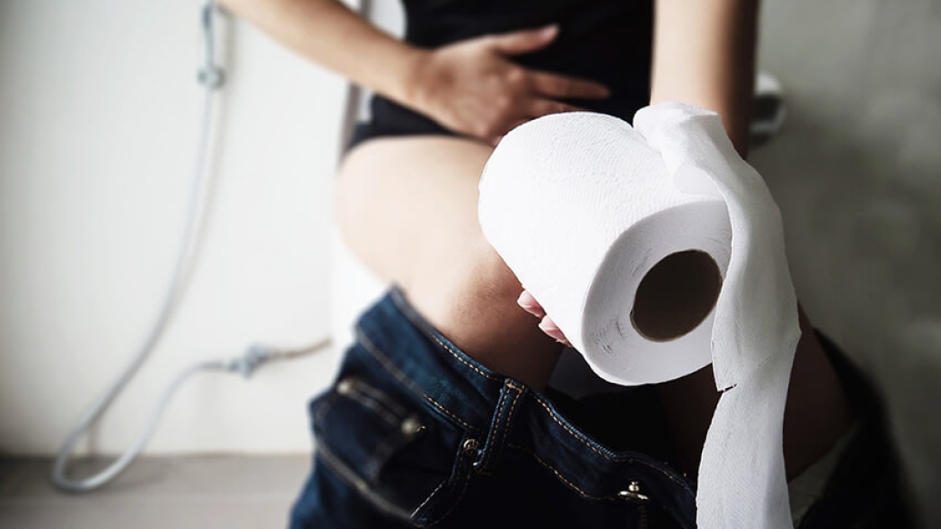 Women sitting on toilet holding stomach and a roll of toilet paper