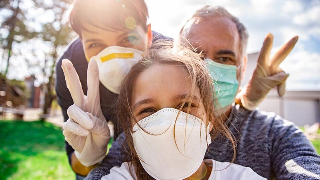 mom, dad and daughter taking selfie outside with peace signs and masks on