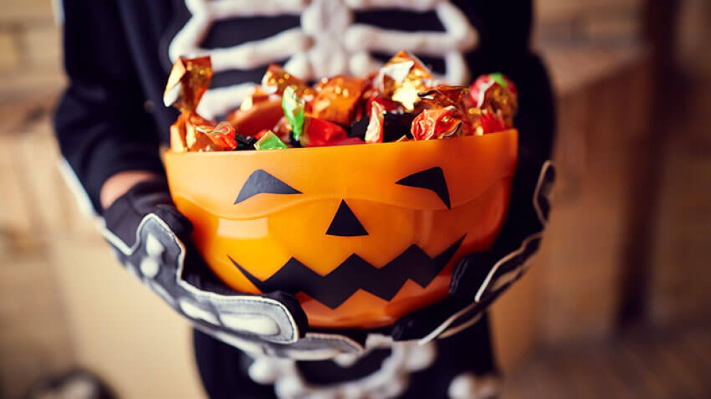 Kid holding pumpkin bowl of candy in skeleton costume