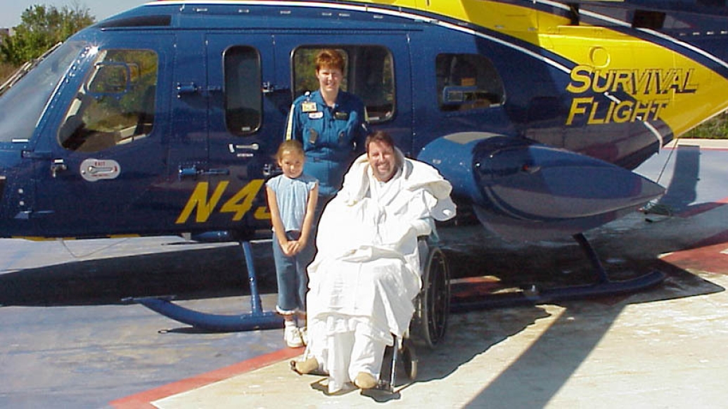 survival flight patient and daughter with employee in front of yellow and blue Michigan helicopter