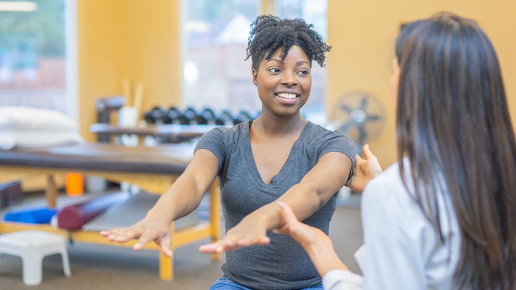 woman stretching out arms and a female physical therapist holding her one arm and talking with her