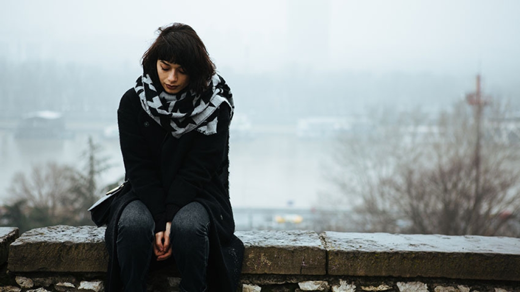 young woman lookin down at the ground wearing black on a foggy day